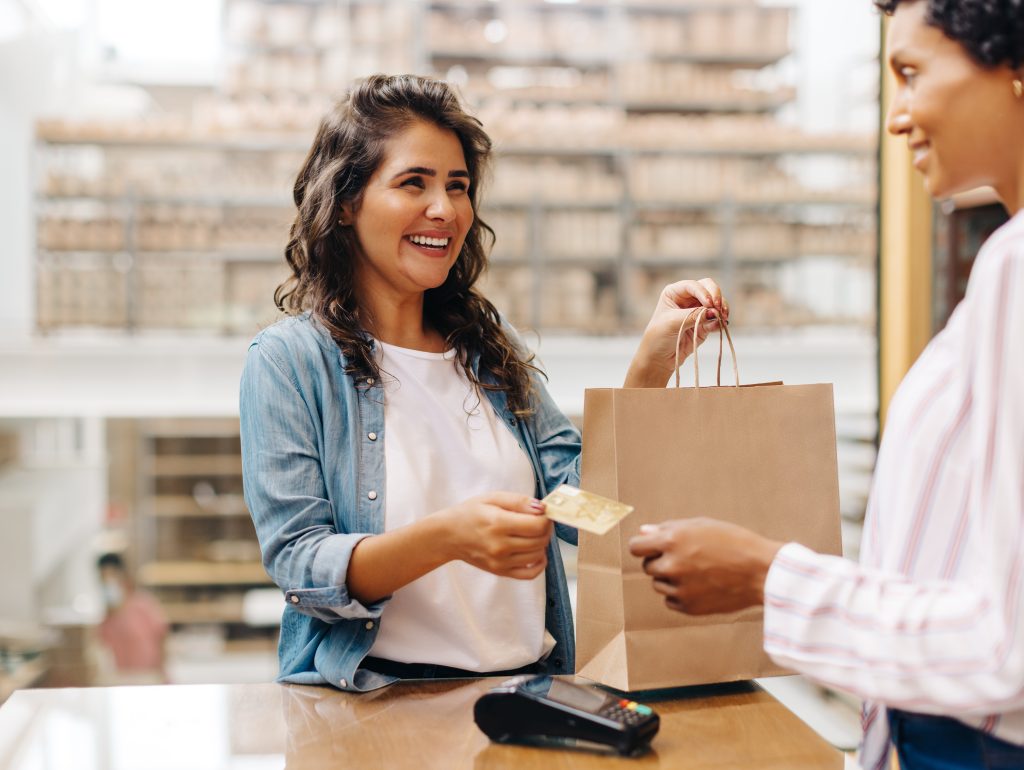 Happy female customer paying her bill with a credit card in a ceramic store. Cheerful young woman smiling happily while shopping from a local female-owned small business.